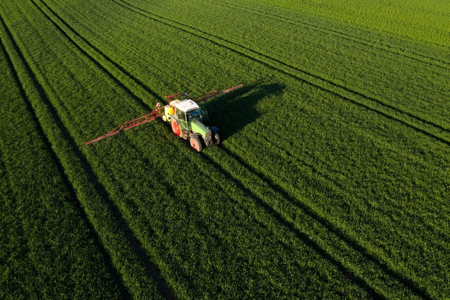 web_aerial_view_of_a_tractor_spraying_green_field_in_sunlight