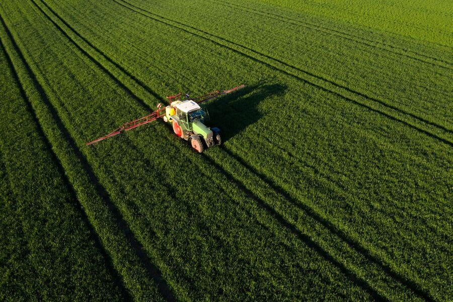 web_aerial_view_of_a_tractor_spraying_green_field_in_sunlight